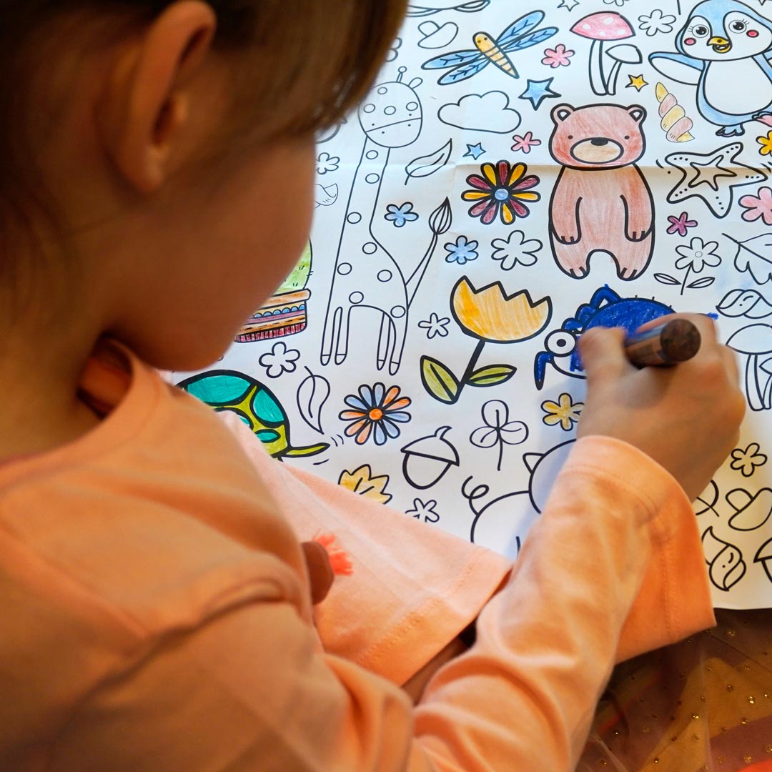 Kind malt Figuren auf der Ausmal-Tischdecke aus