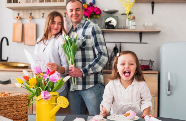 funny-daughter-making-cupcake-near-parents-with-greeting-card